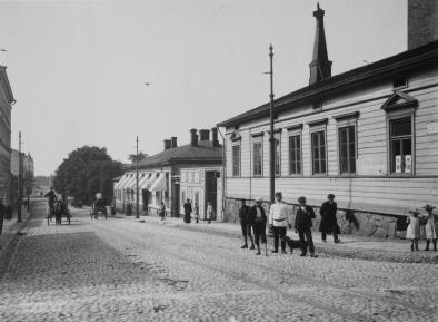 People standing on a stone road in an urban surroundings. Year is 1907.